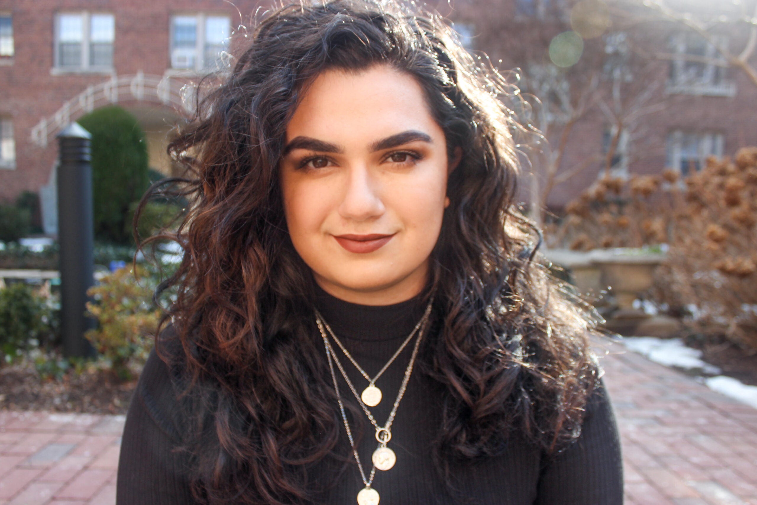 Headshot of Alanna Kronk with brick patio and buildings in the background