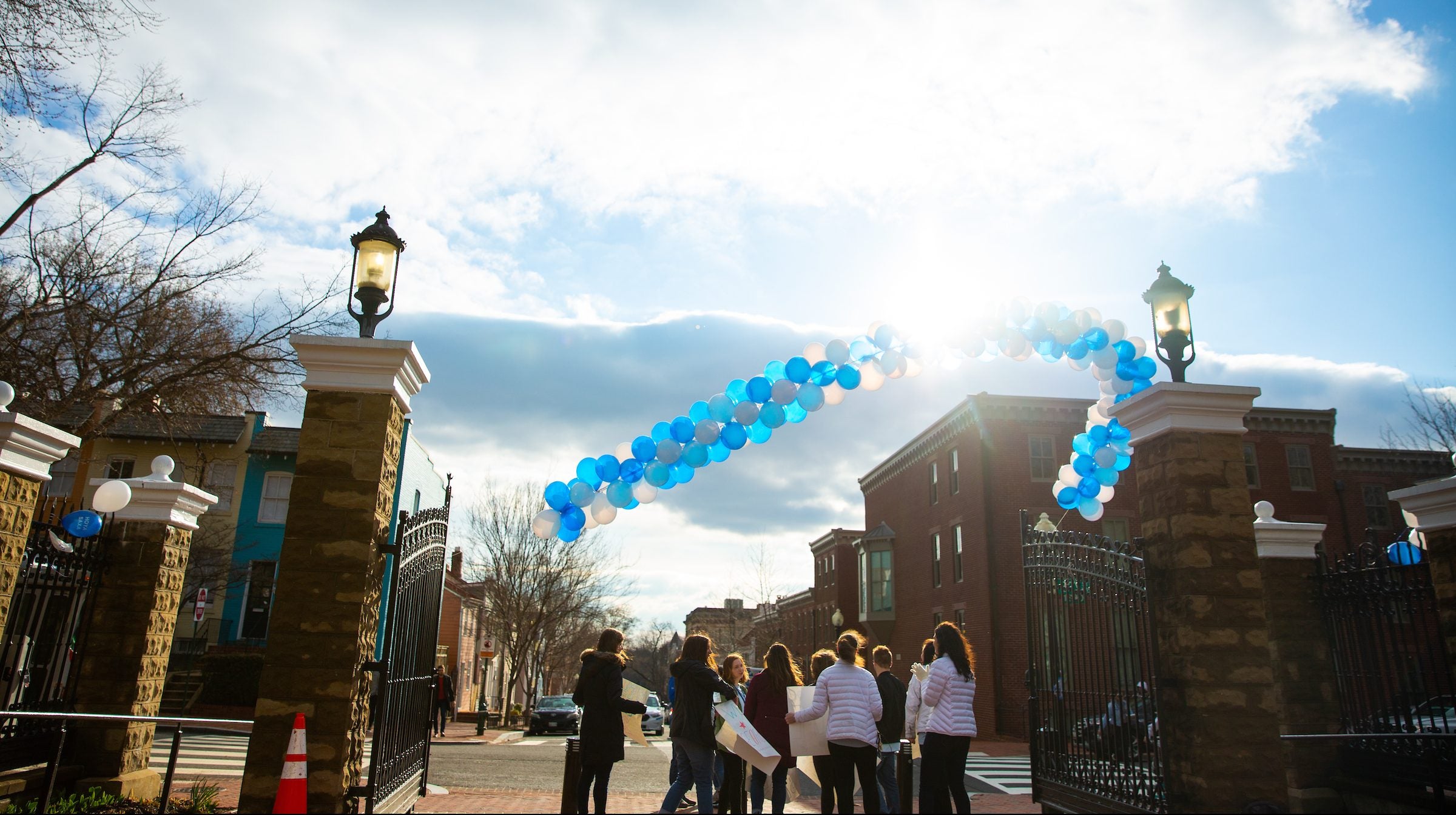 Students with their back turned below a balloon arch in front of a sun flare