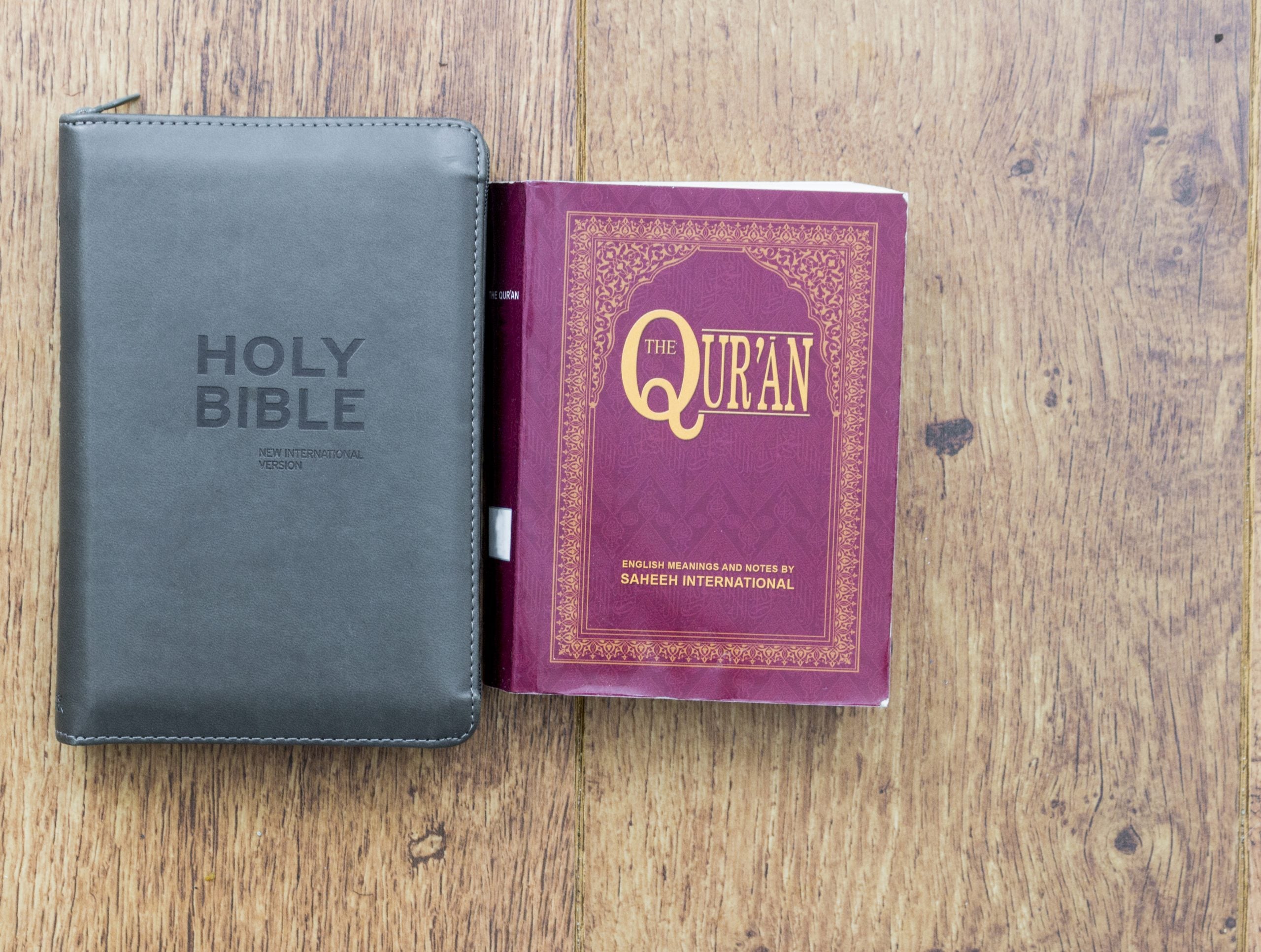 Black Holy Bible next to a Red Qur'an on a wood surface