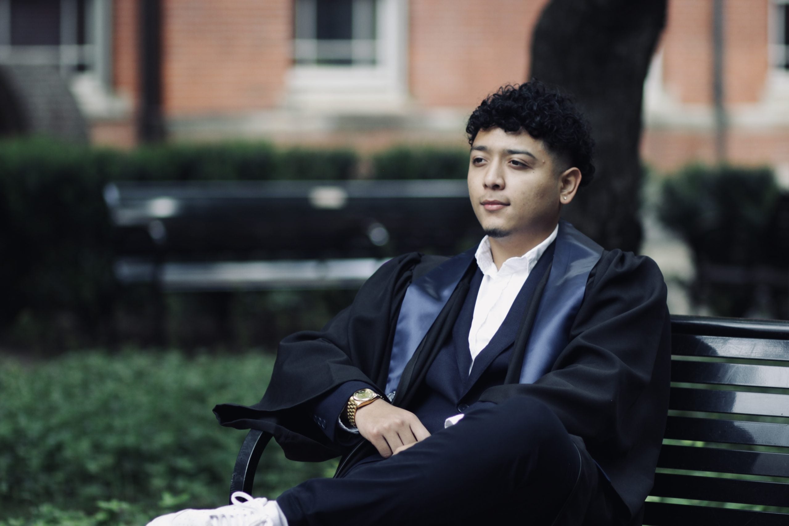 Andy sits on a bench in Dahlgren Quad in his graduation robes