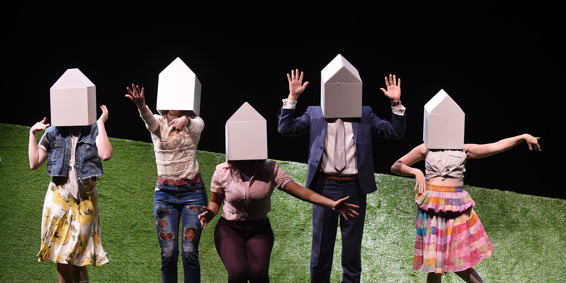 Student actors with houses covering their heads on a grass set