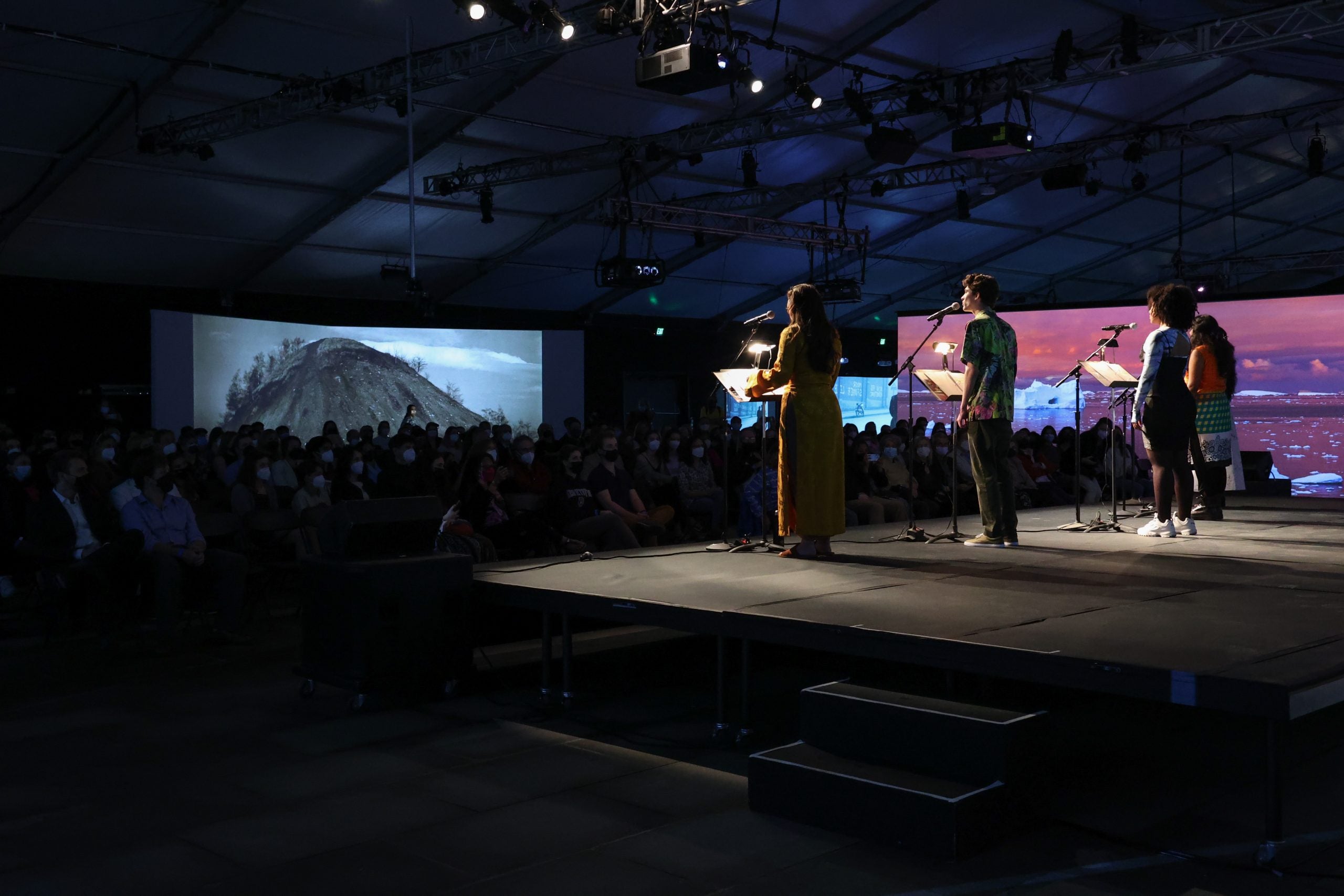 Actors perform on a stage with a projection of mountains behind the audience