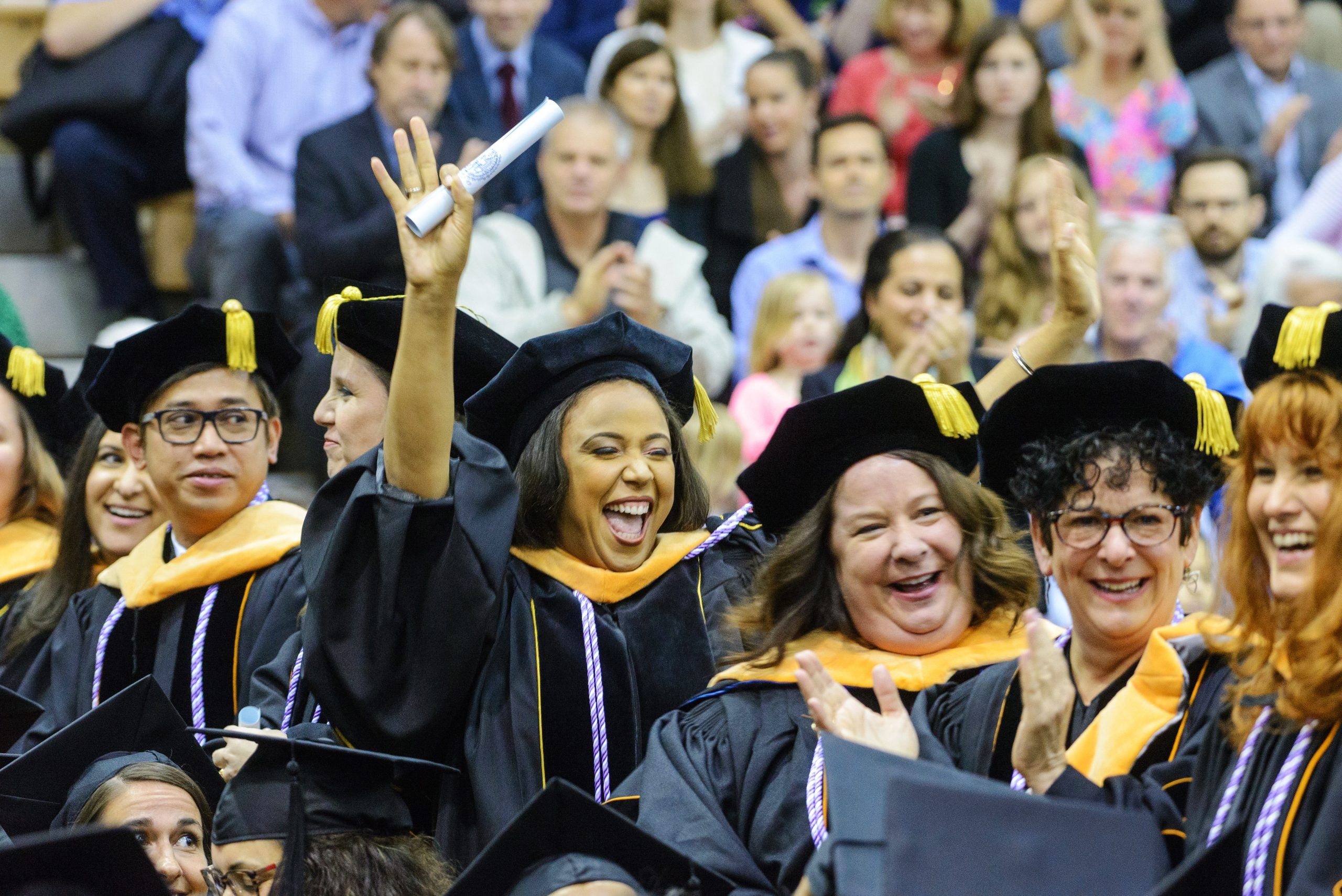 Student wearing graduation attire holding a diploma cheers in a crowd