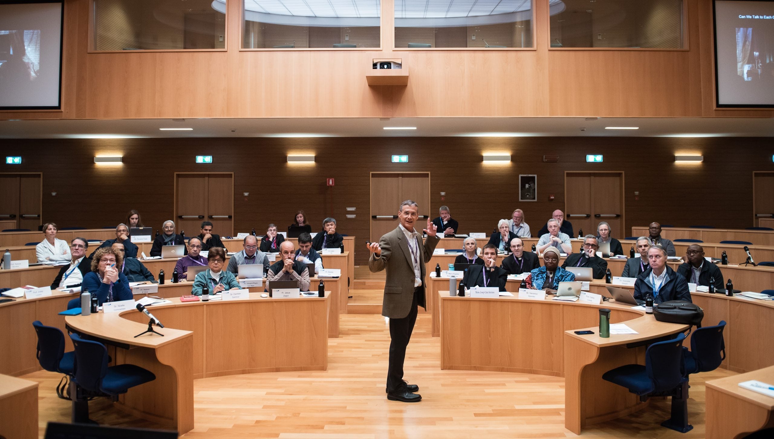 Professor in the middle of a lecture turns to face the camera as adult students watch