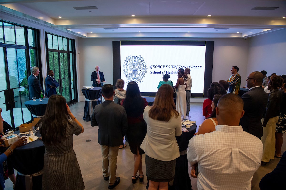 Crowd of people see presentation with a projection of the text "Georgetown University School of Health"