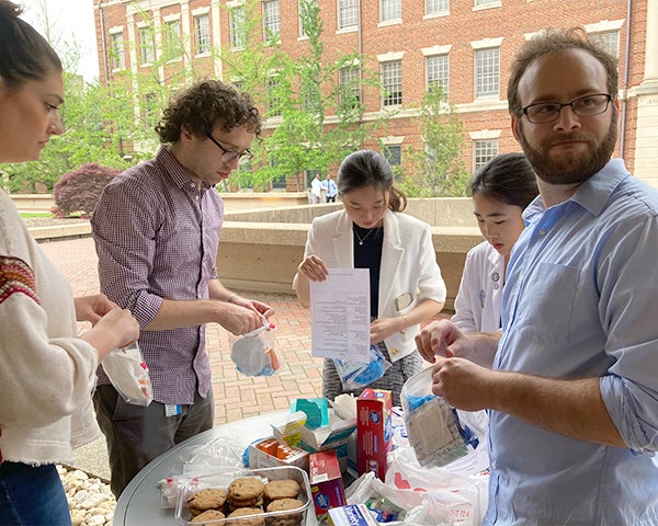 Four medical students assemble first aid kits on a table outside.