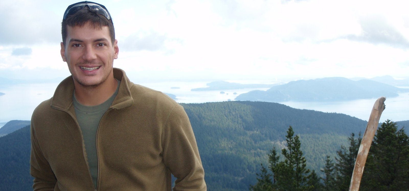 Austin Tice wears a dark khaki-colored zip up in front of mountains