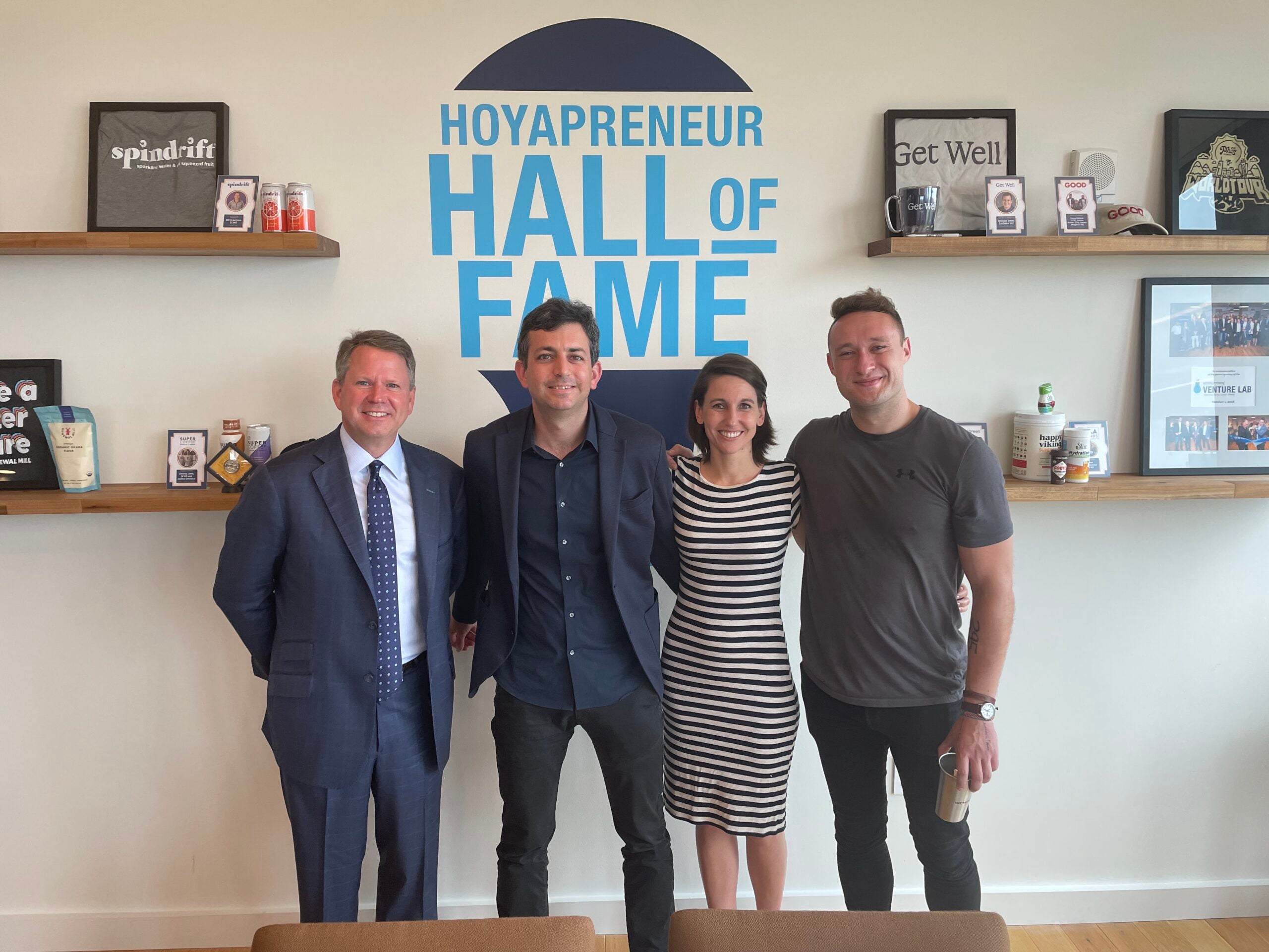 Four Georgetown community members stand in front of a sign painted on a wall that says "Hoyapreneur Hall of Fame"