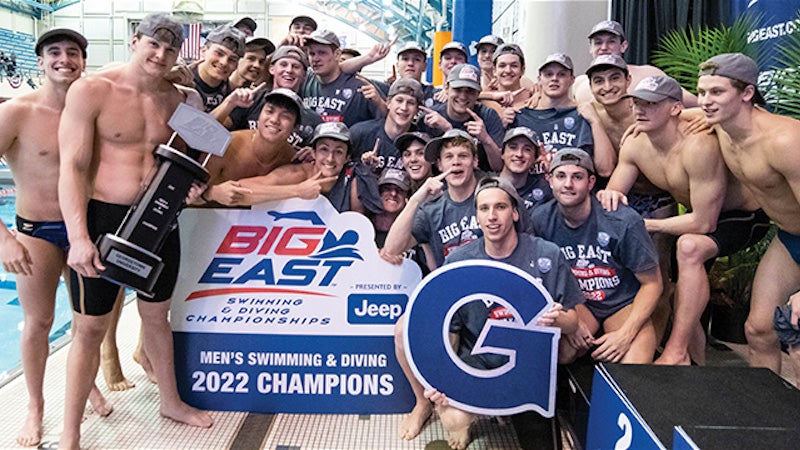 Men in bathing suits celebrating around a Georgetown "G" and "2022 Champions" sign