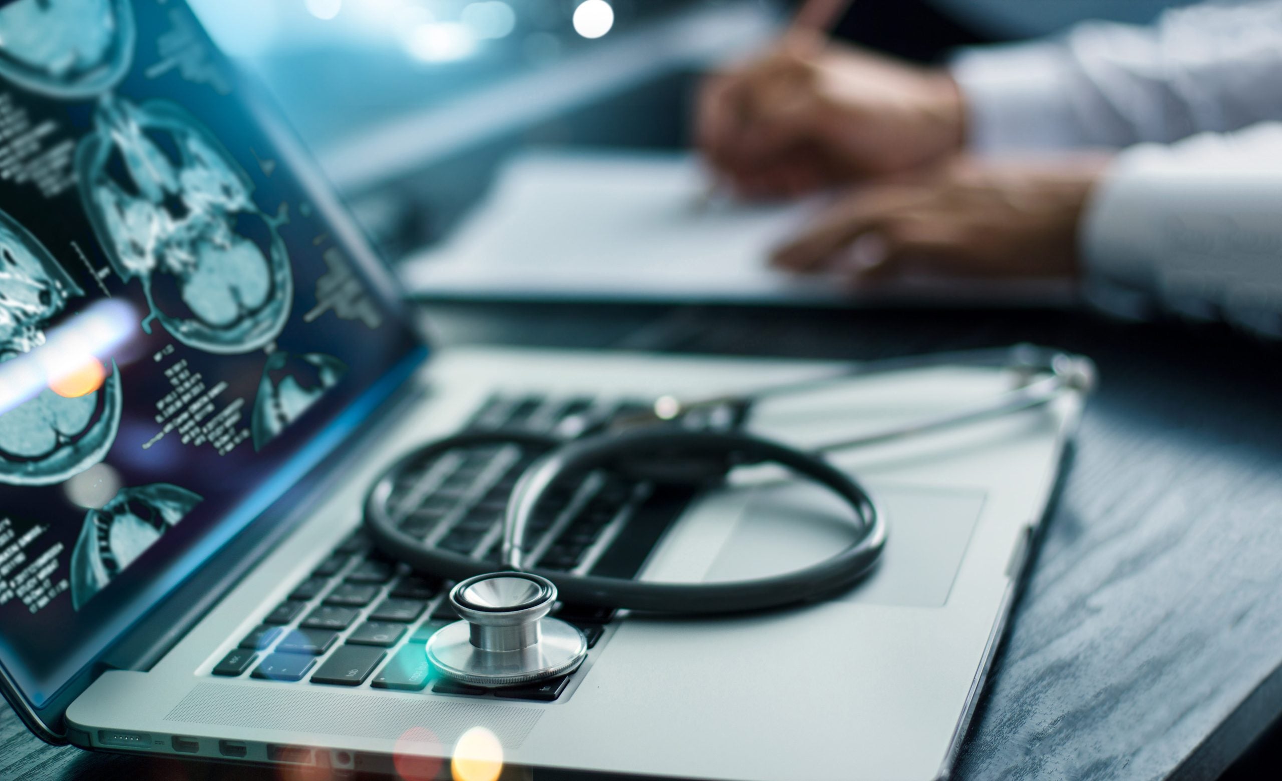 A close up of a laptop screen with brain scans and a stethoscope lying on the keyboard.