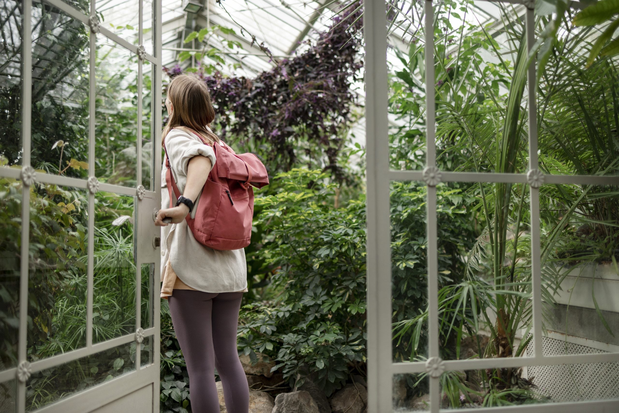 Rear view of a female student visiting local botanical garden, walking through the entrance and admiring the lush nature in the middle of the city