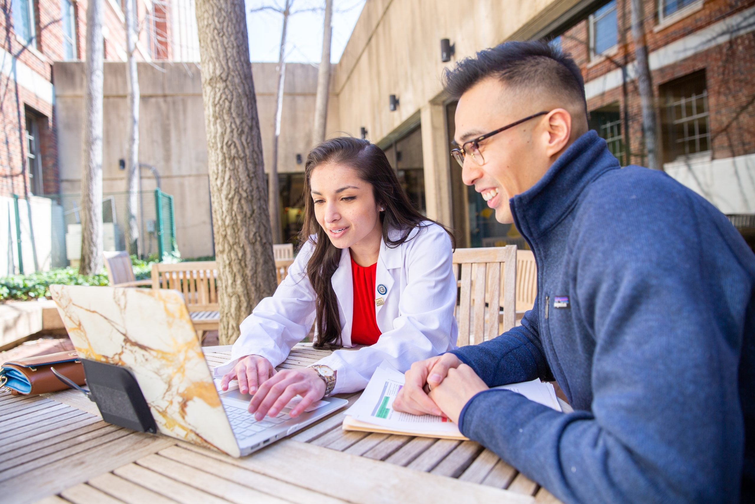 Two medical students look at a laptop at a table outside.