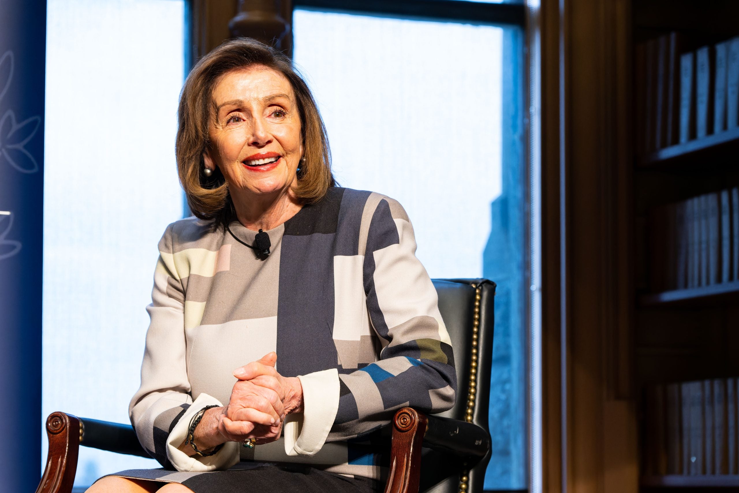 Nancy Pelosi smiles with clasped hands on stage at Riggs Library