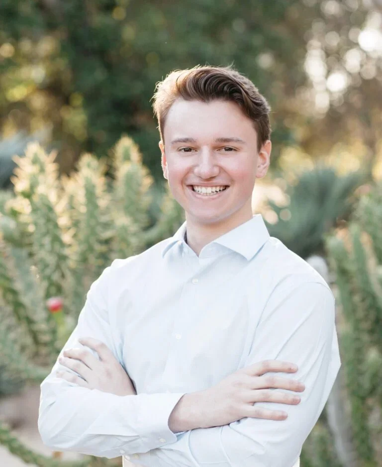 Brendan Foody (B'25) smiles with arms crossed against a background of plants.