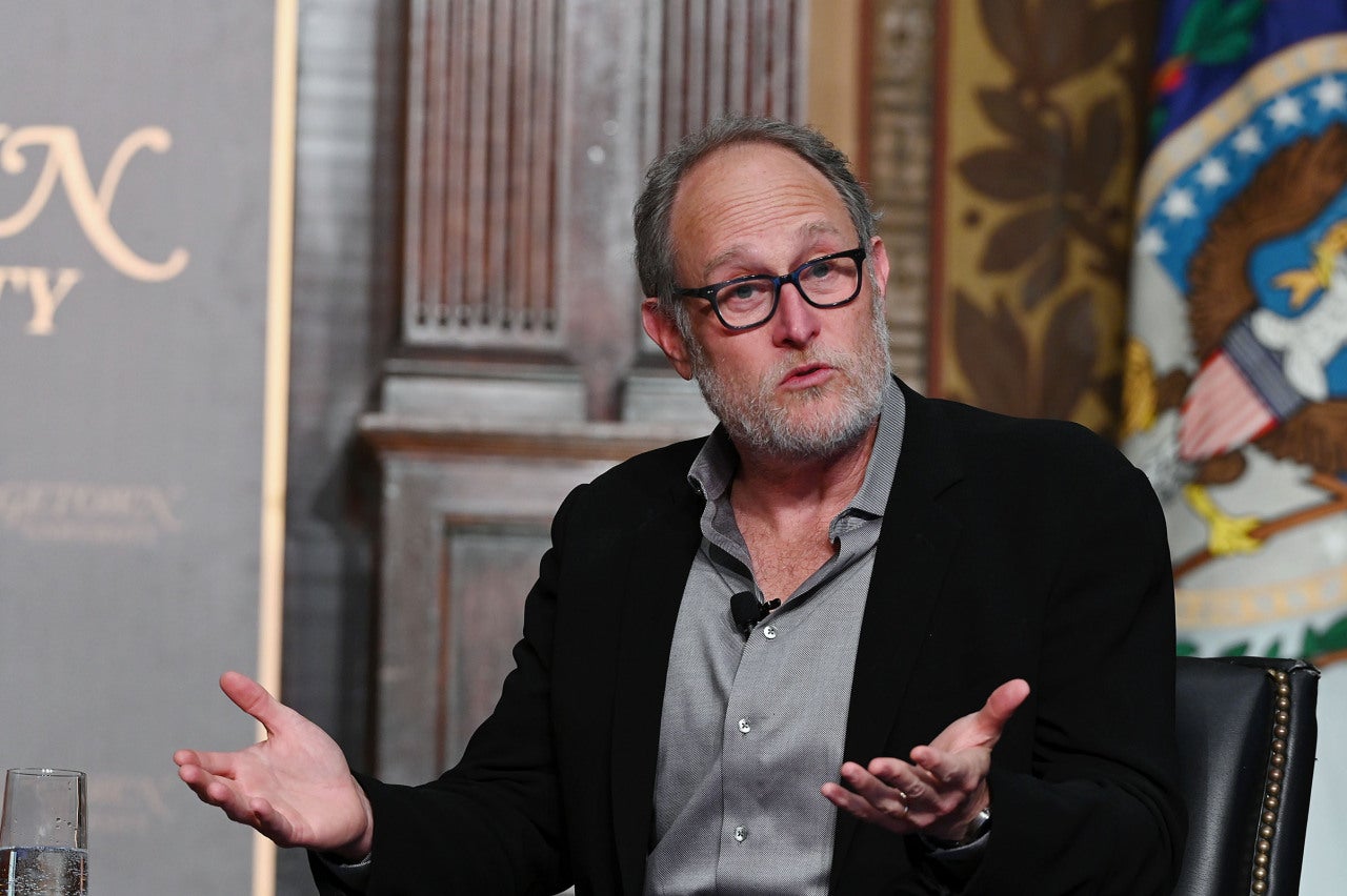 Jon Turteltaub gestures with open hands on stage at Gaston Hall.