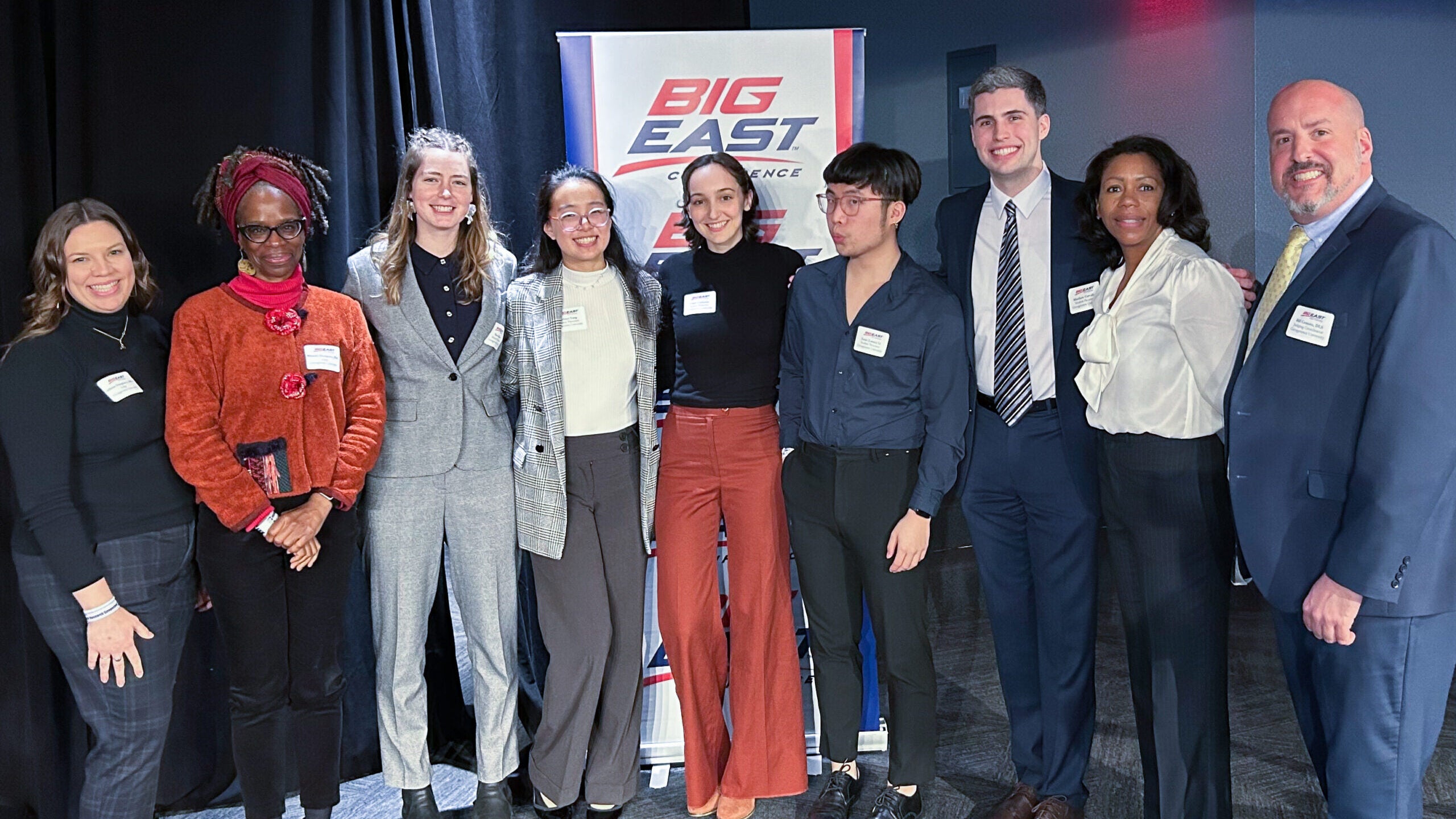 9 people -- including the poster presenters -- pose in front of a sign that reads "Big East Research Symposium"