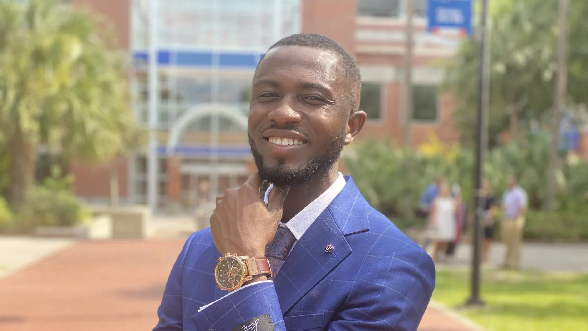 Crispin Beyogle (LAS'23) smiles with hand on chin in a blue suit