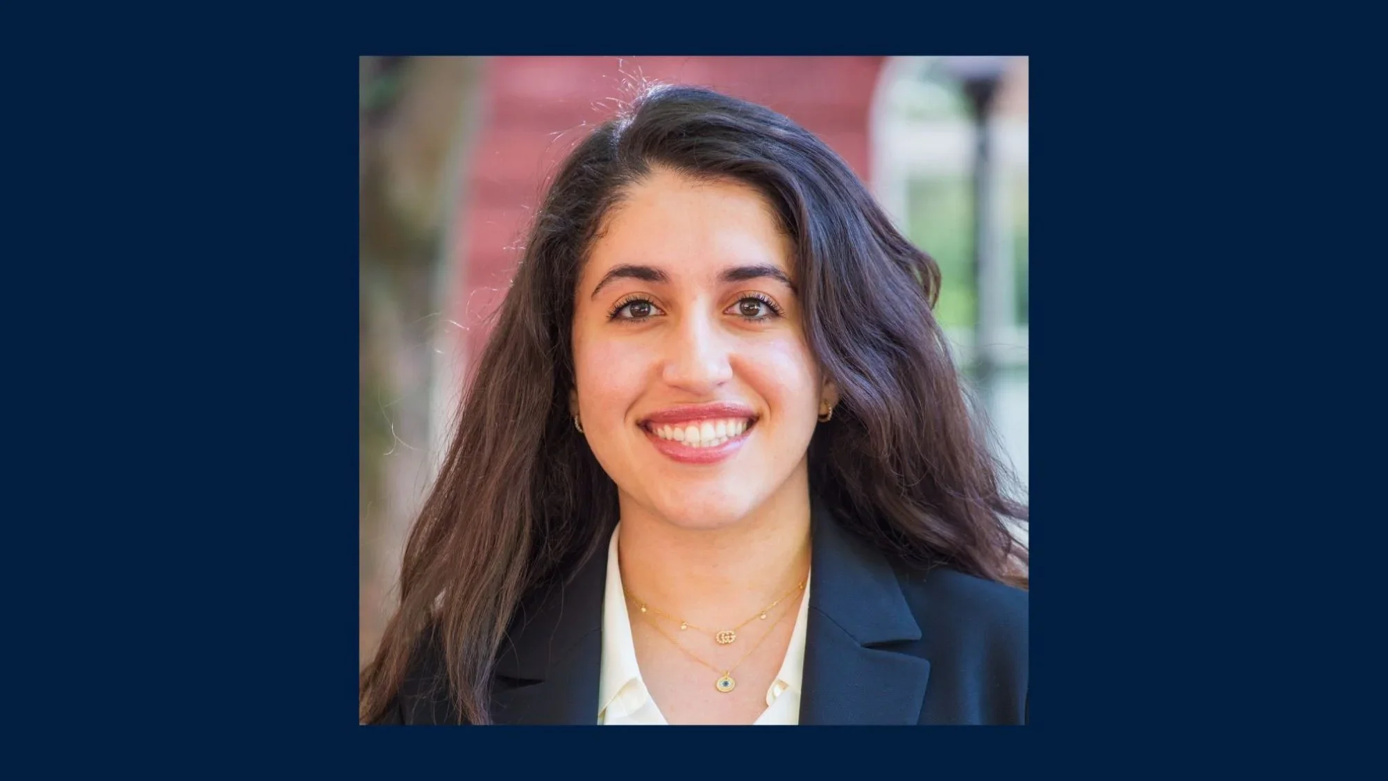 Shelby Emami, a graduate student in the School of Foreign service, smiles at the camera. She wears a blue blazer and a white shirt.