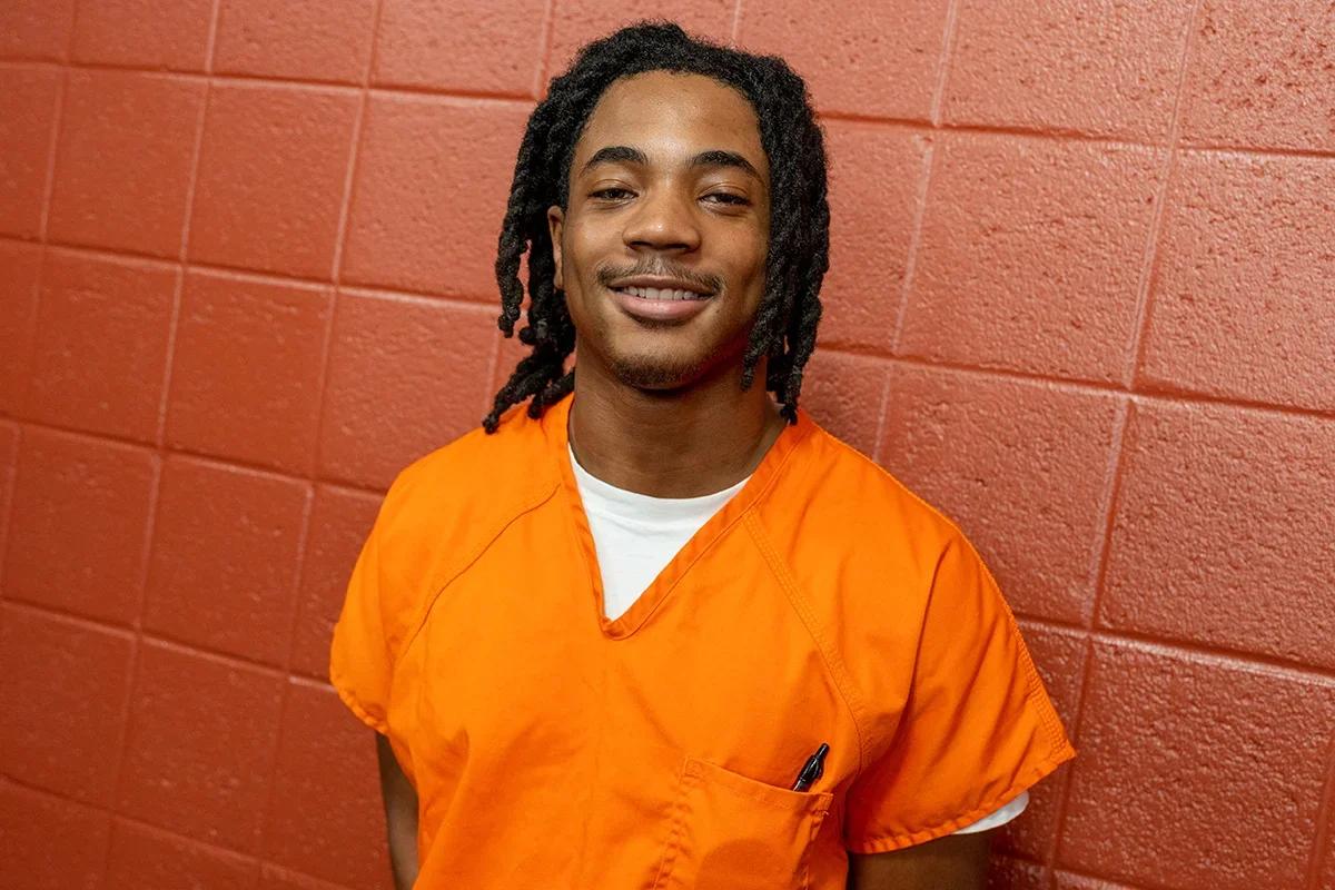 Georgetown Prison Scholar Keonte Lewis wears an orange jumpsuit in the DC jail, smiling at the camera.