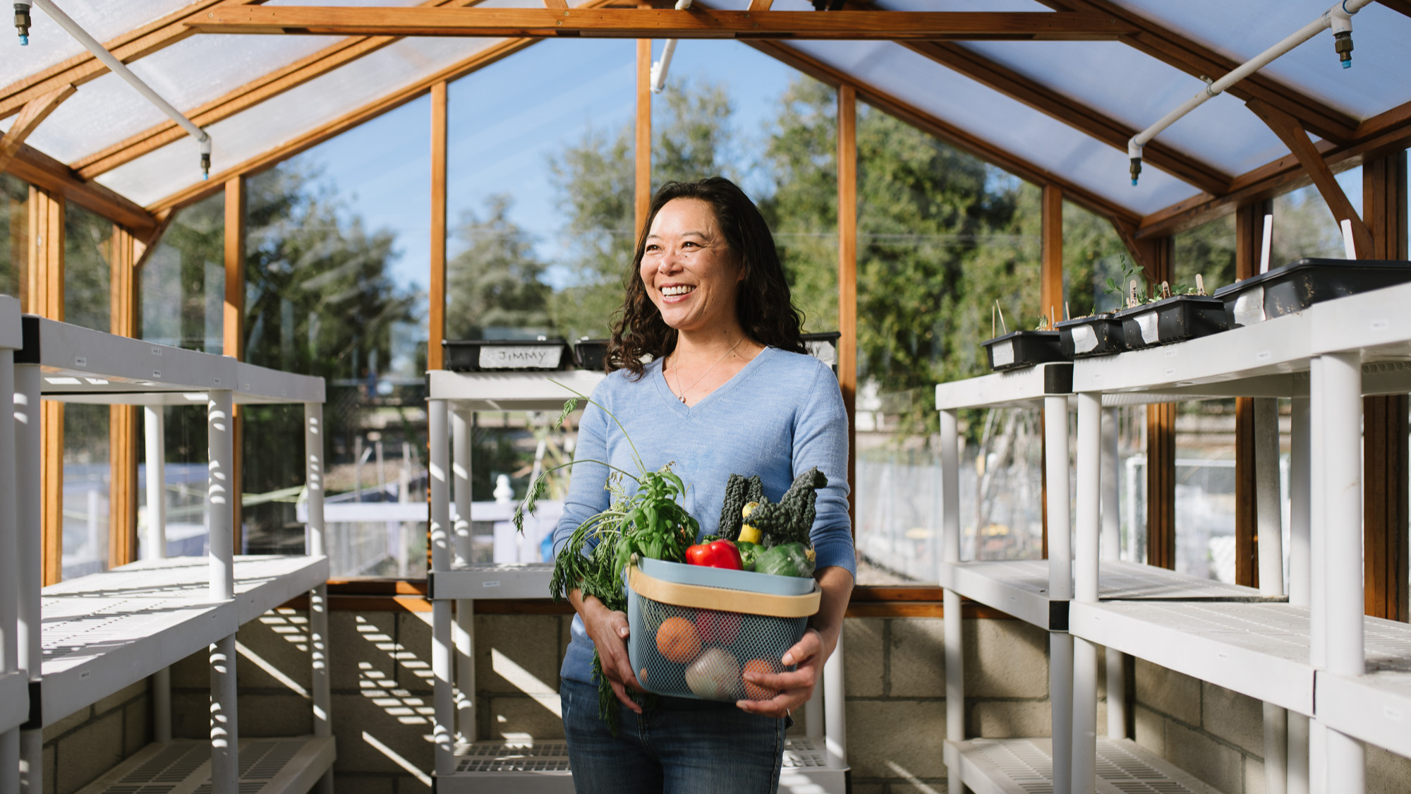 Naomi Hansen (B'95) carries a basket of produce and stands outside in her greenhouse.