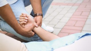 One stranger checks the pulse of another stranger, who&#039;s laying on the ground.