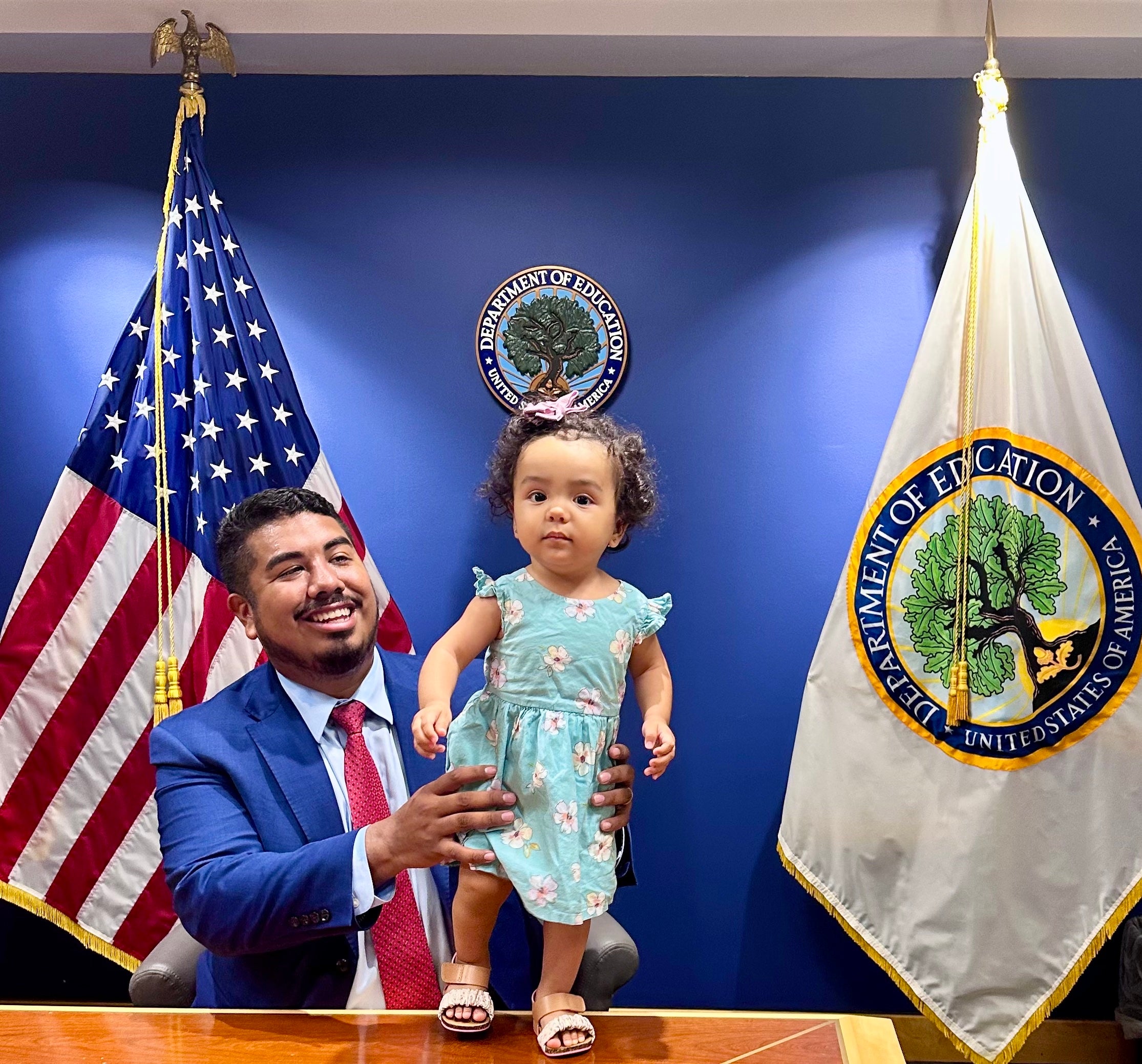 Adan Gonzalez (C'15) holds up his daughter on the podium of a conference room at the U.S. Dept. of Education.