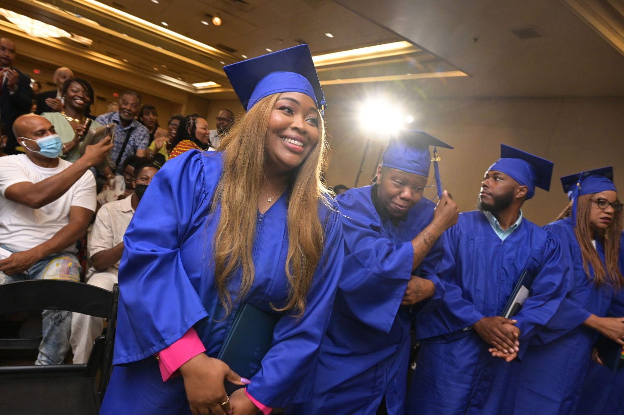 A female graduate of the Pivot Program wearing a blue cap and gown smiles as she graduates.