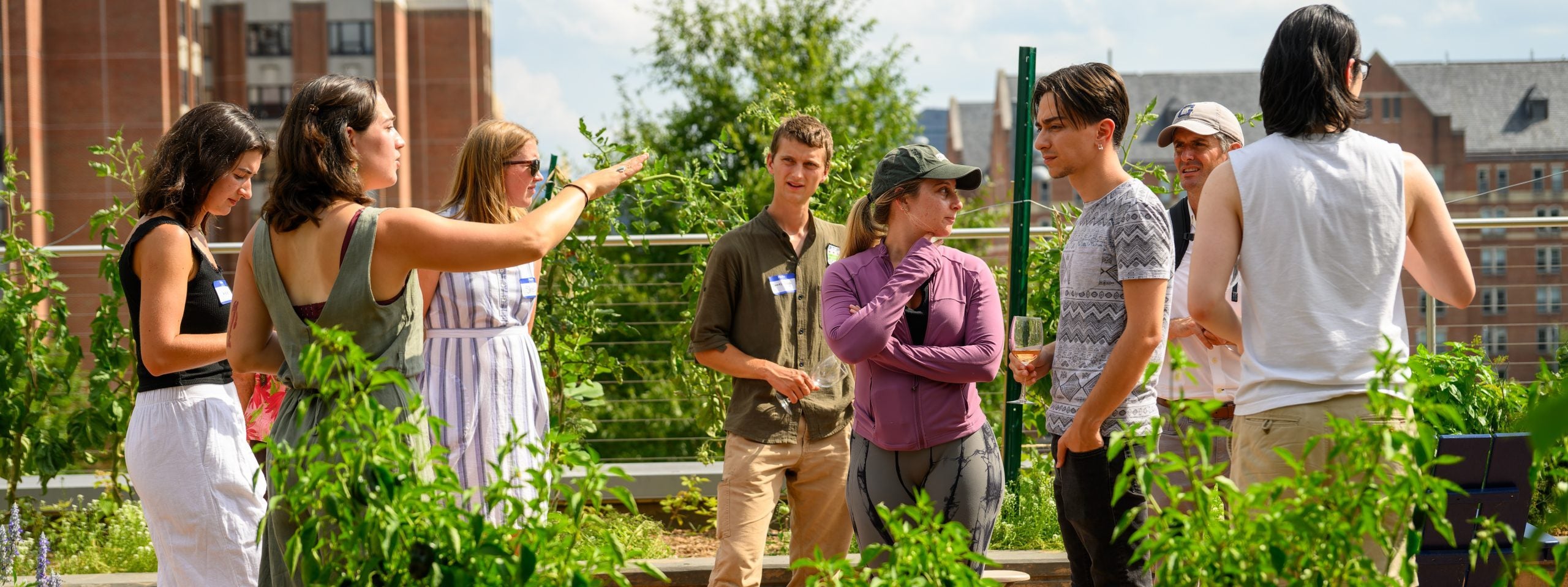 Individuals gathered in front of garden plants, outside.