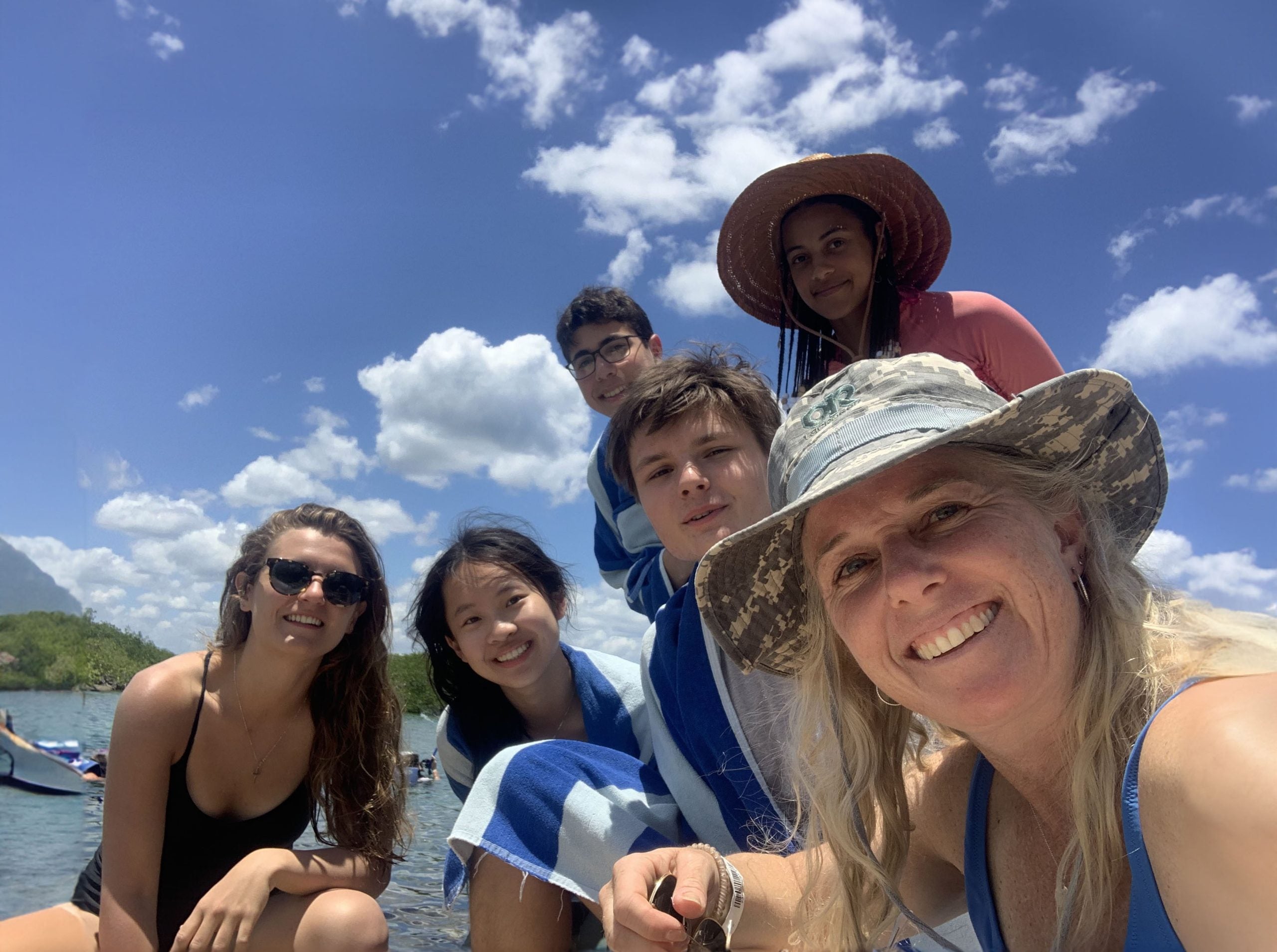 A group of students and a faculty member pose for a selfie with a beach and blue sky in the background.