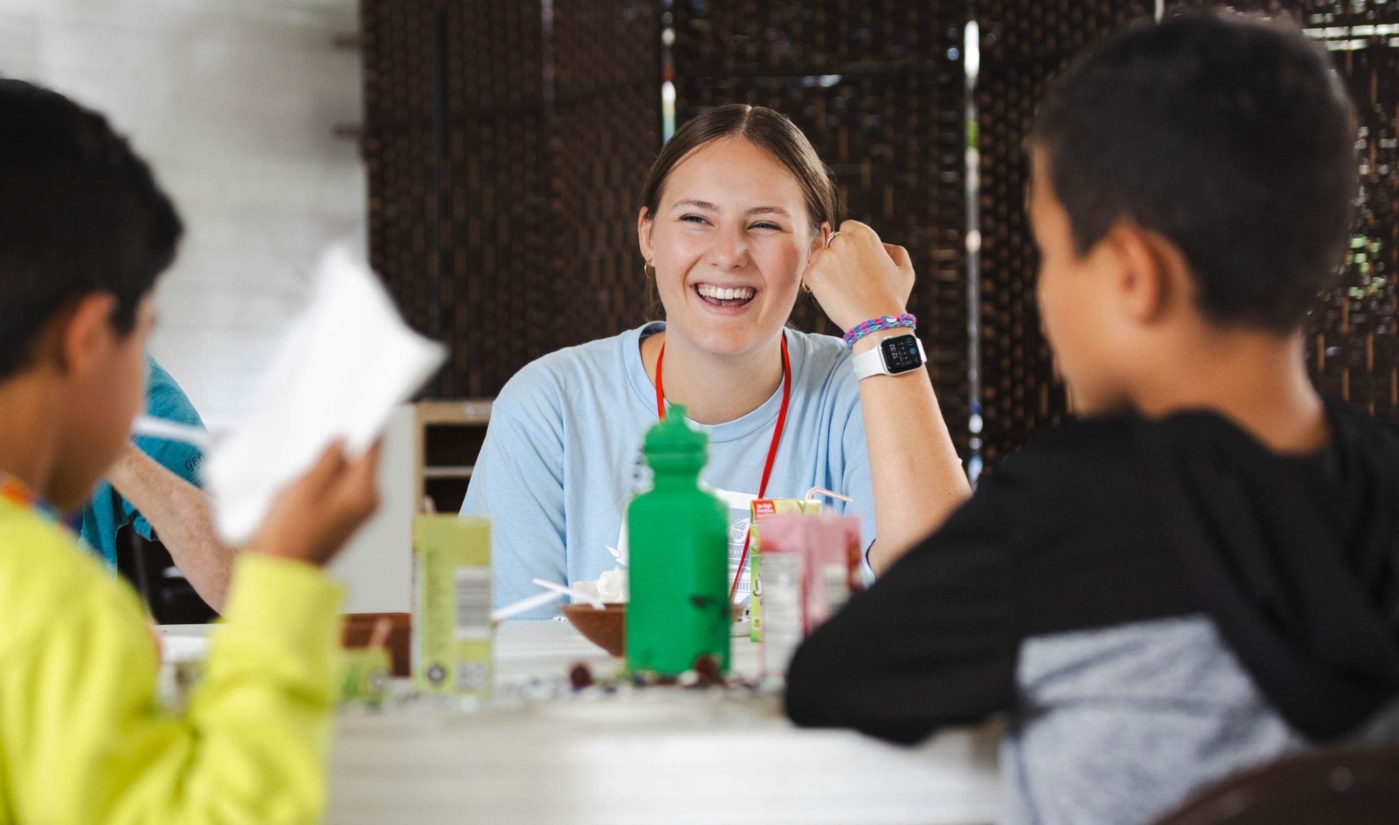 A young woman smiles while sitting with two boys at a table.