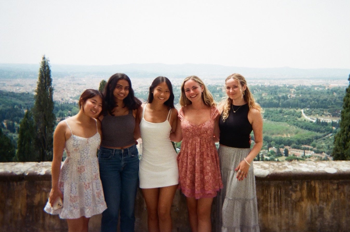 Five girls stand smiling with the landscape of Italy behind them