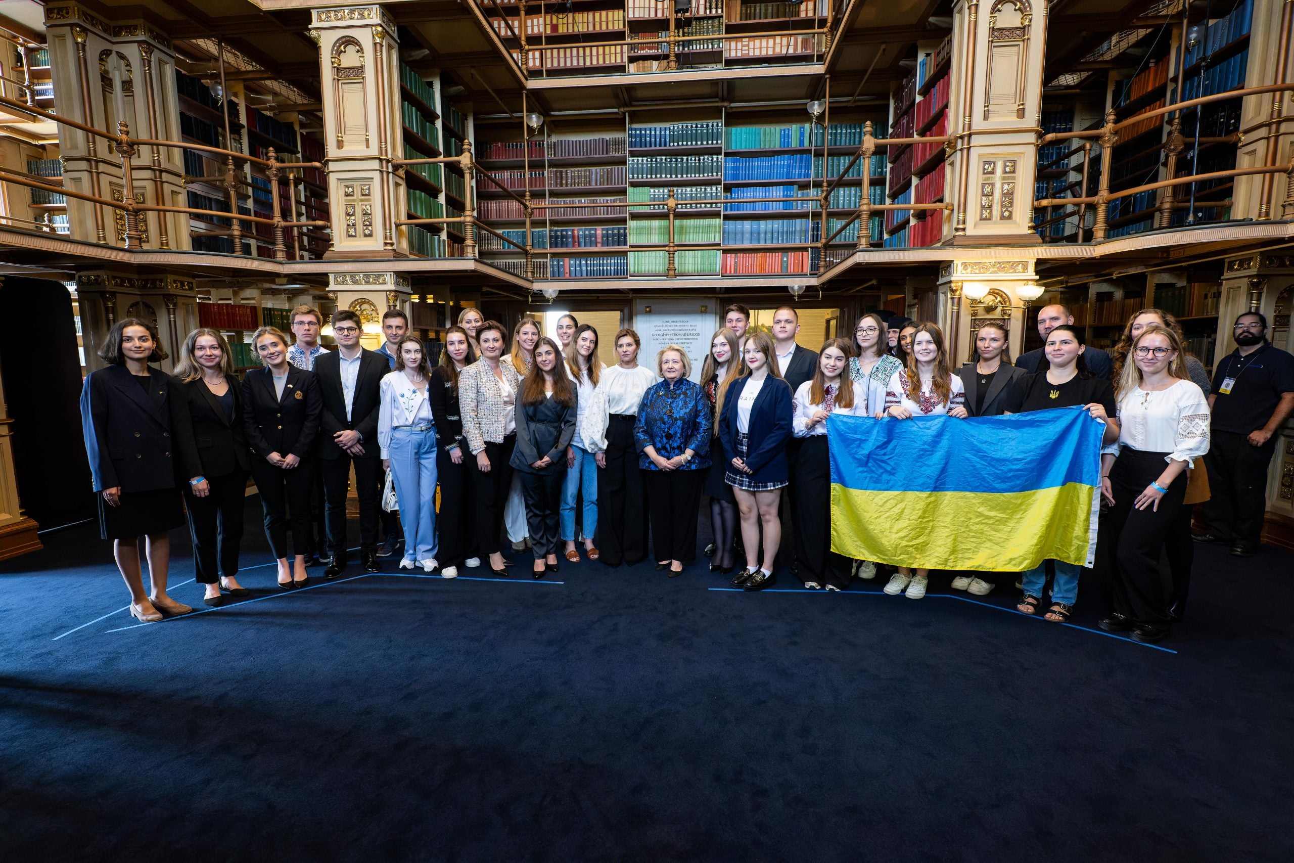 A group of Ukrainian students pose with the First Lady of Ukraine in a Georgetown library. One student holds up the yellow and blue Ukrainian flag.