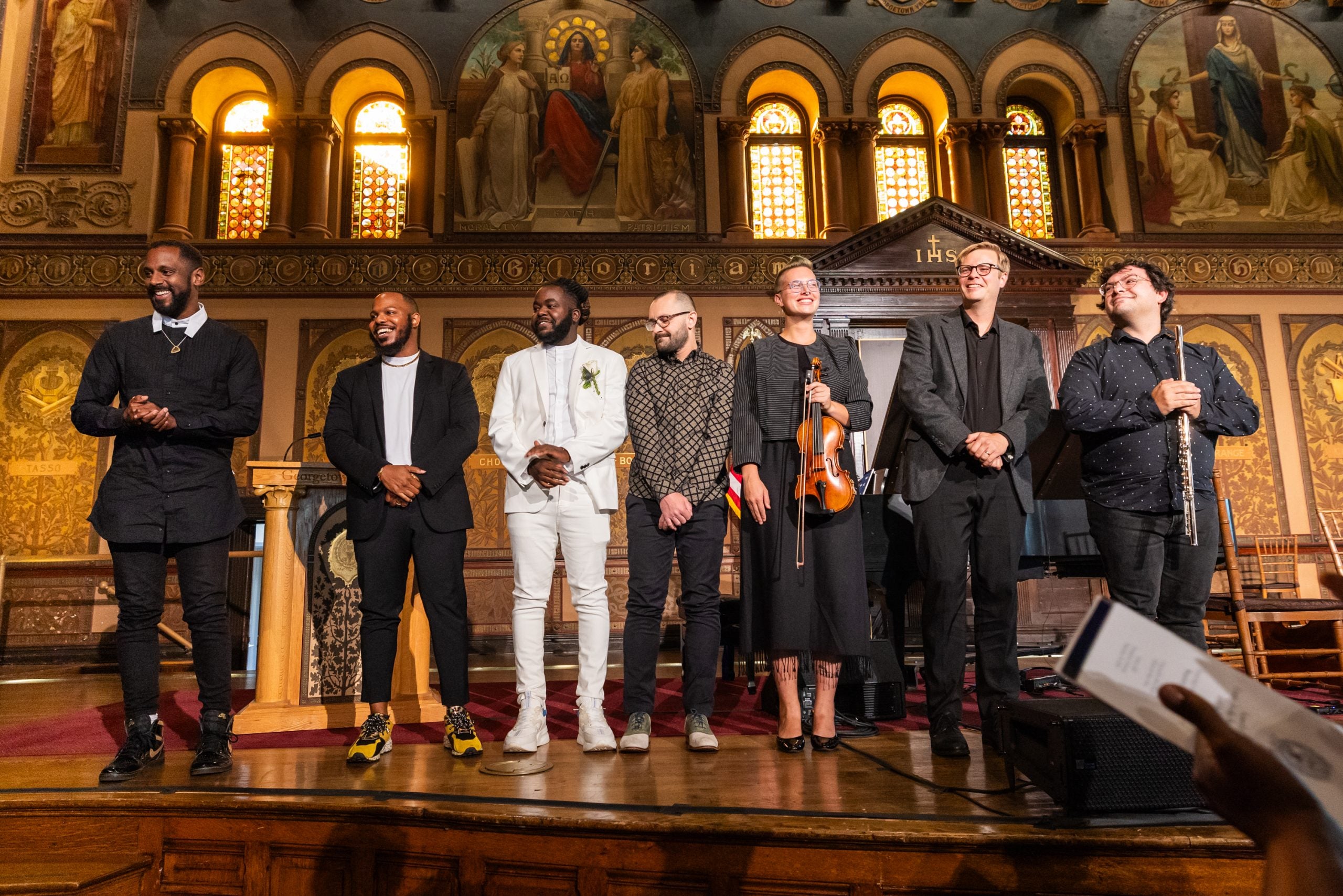 A group of musicians stand on stage of Georgetown's Gaston Hall after a live performance.