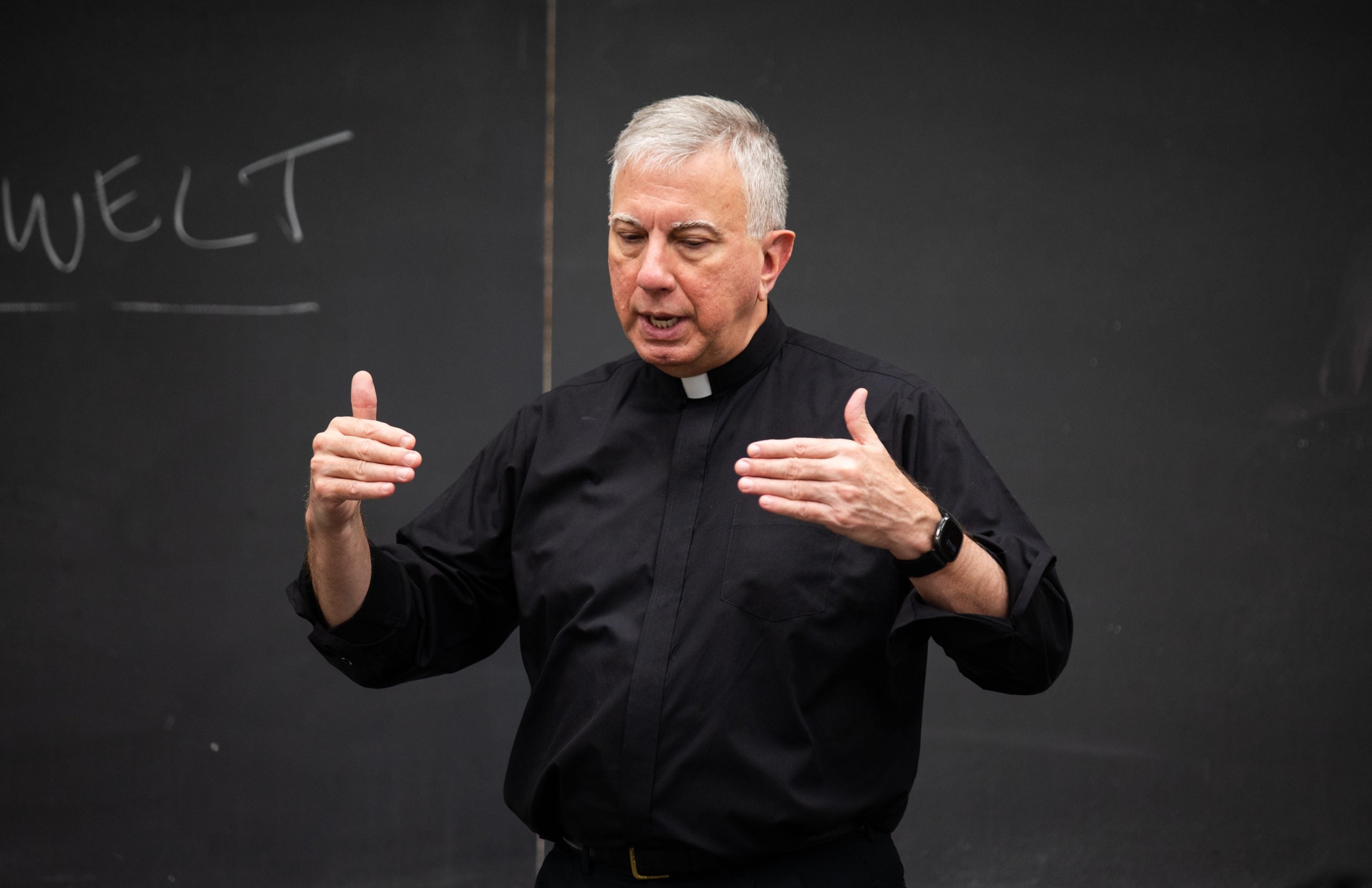 A Catholic priest teaching in front of a chalkboard in a classroom