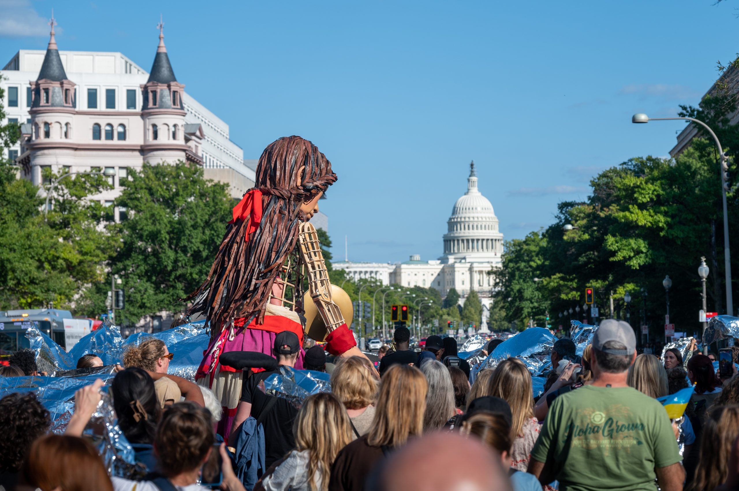 Little Amal, a puppet made to resemble a 10-year-old Syrian refugee, walks in a crowd toward the U.S. Capitol in the distance.