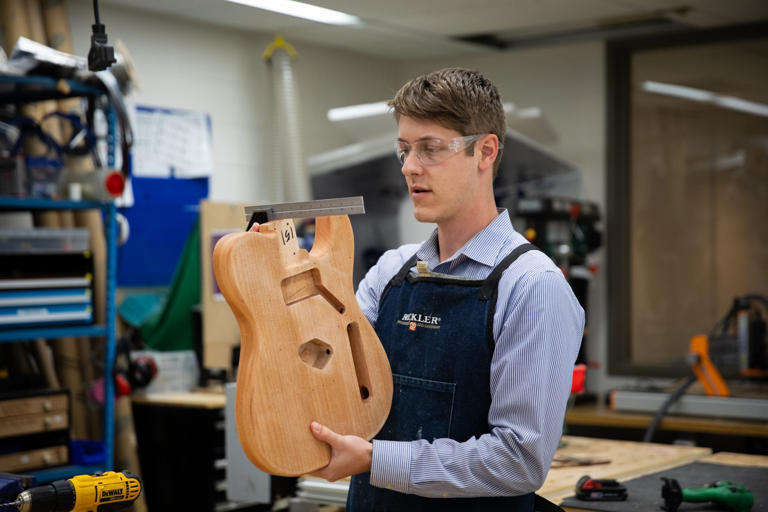 David Strout wears protective glasses and holds up the bottom of a wooden guitar in the Maker Hub on Georgetown's campus.