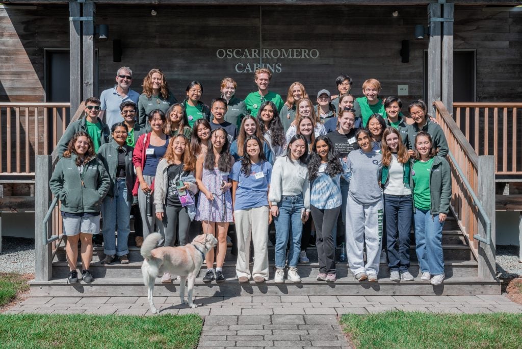 A group of students and a dog stand at the stairs of the retreat center, smiling at the camera