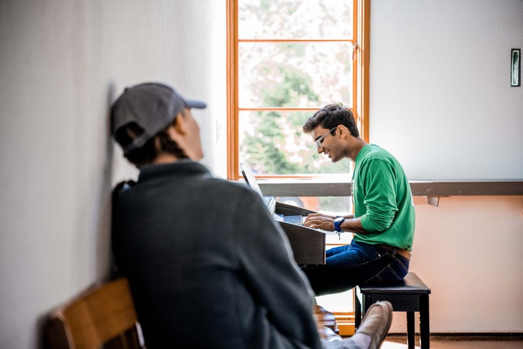 One student watches as another performs a song at the piano