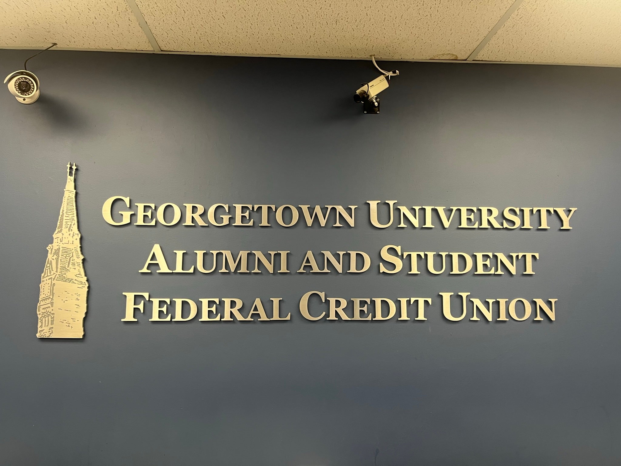 A wall with gold lettering introducing the Georgetown University Alumni and Student Federal Credit Union, with a gold Healy Tower next to it