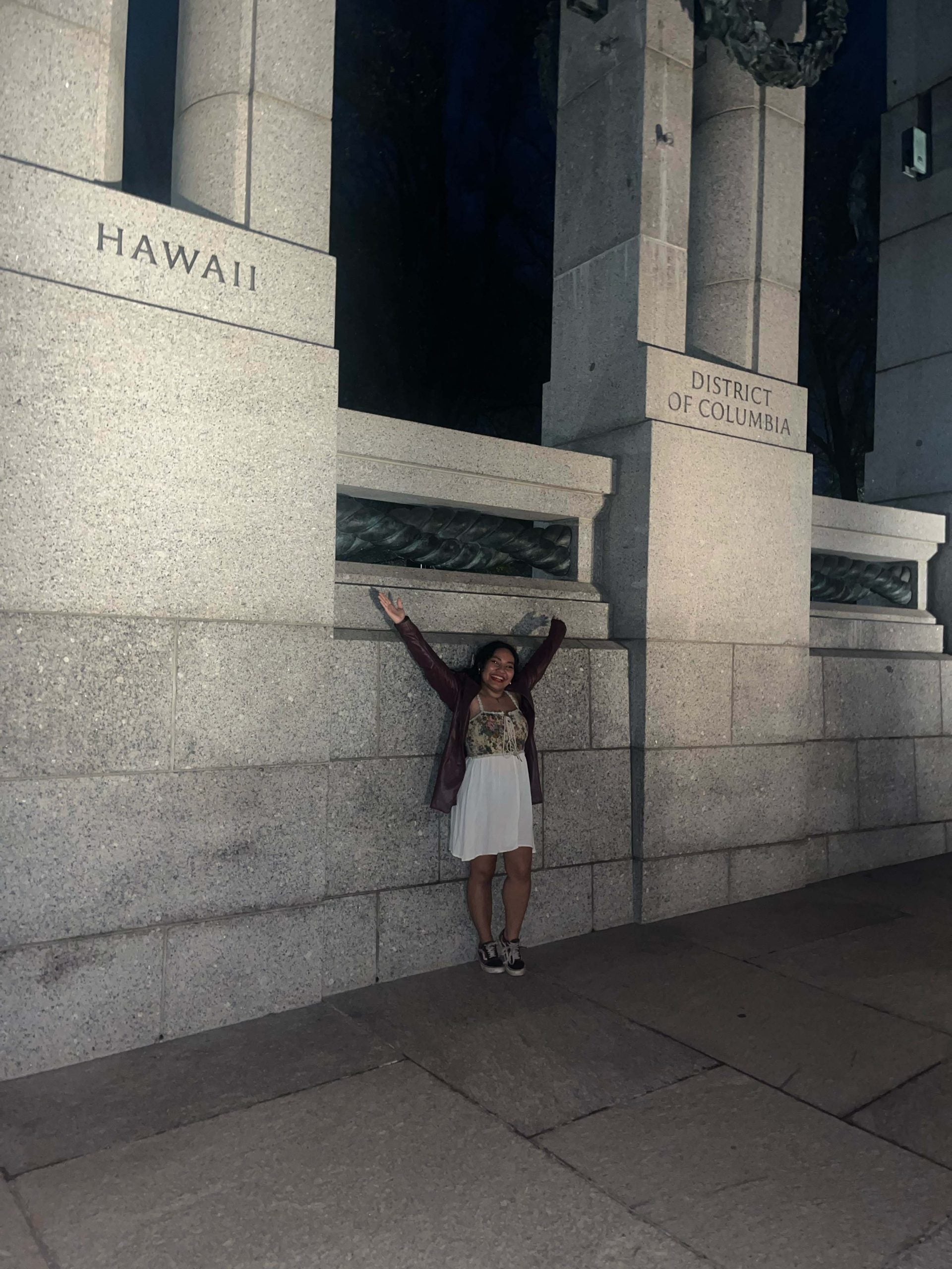 Mara stands with her arms wide between the Hawaii and DC monuments at the World War 2 Memorial