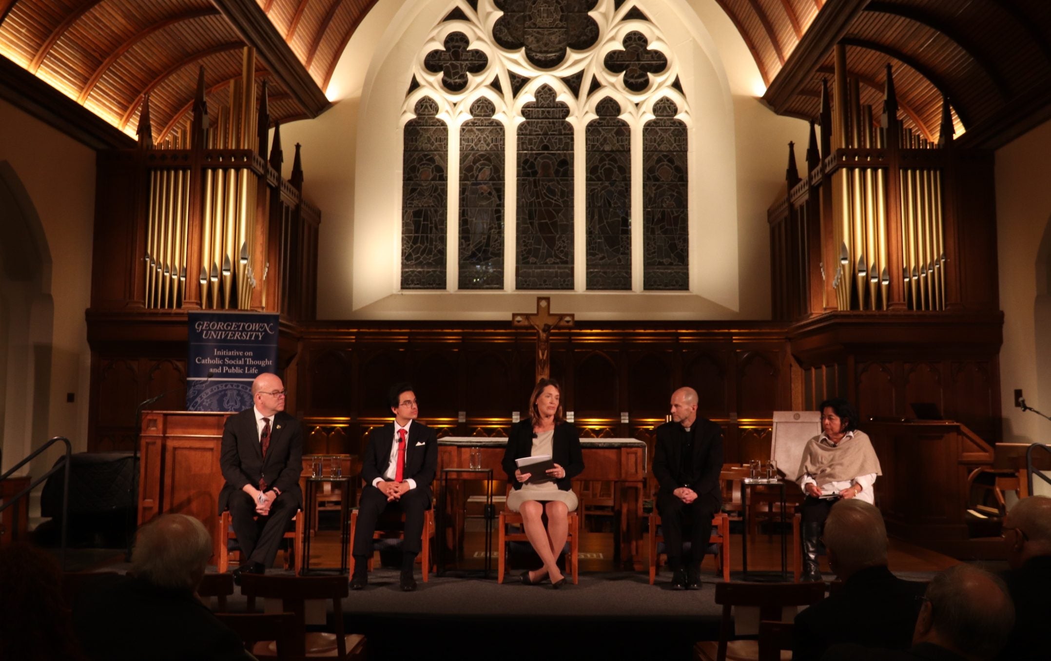 A panel of four people speak in a dimly lit chapel