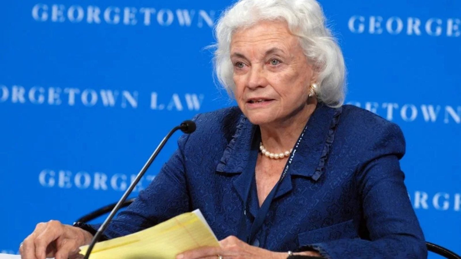 The late Supreme Court Justice Sandra Day O&#039;Connor sits in front of a blue background that says &quot;Georgetown Law&quot;