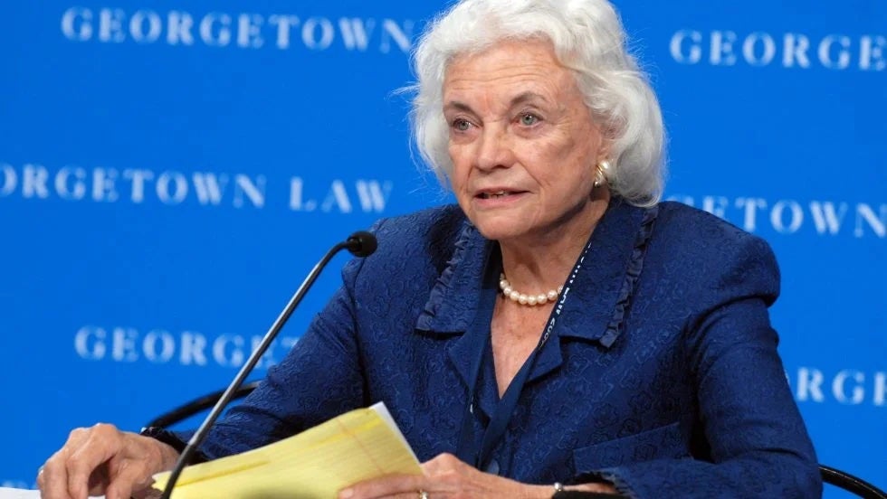 The late Supreme Court Justice Sandra Day O'Connor sits in front of a blue background that says "Georgetown Law"