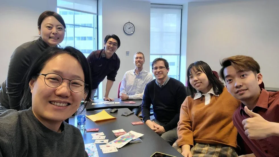 A group of students take a selfie around a table in a classroom.