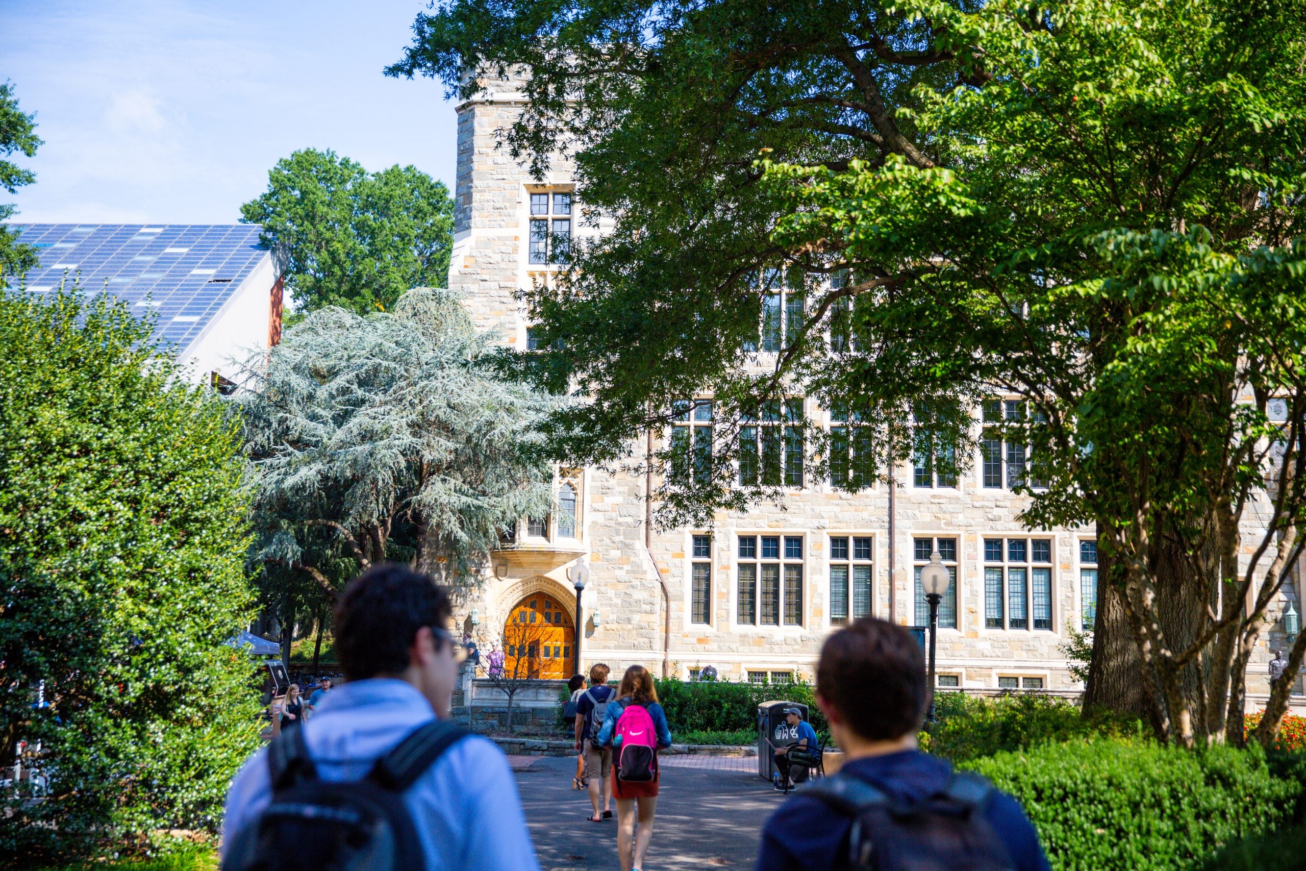 Students on a summer day walk toward a stone building on Georgetown's campus.