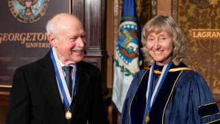 A husband smiles at his wife on stage after they both participated and were honored in Georgetown&#039;s spring faculty convocation.