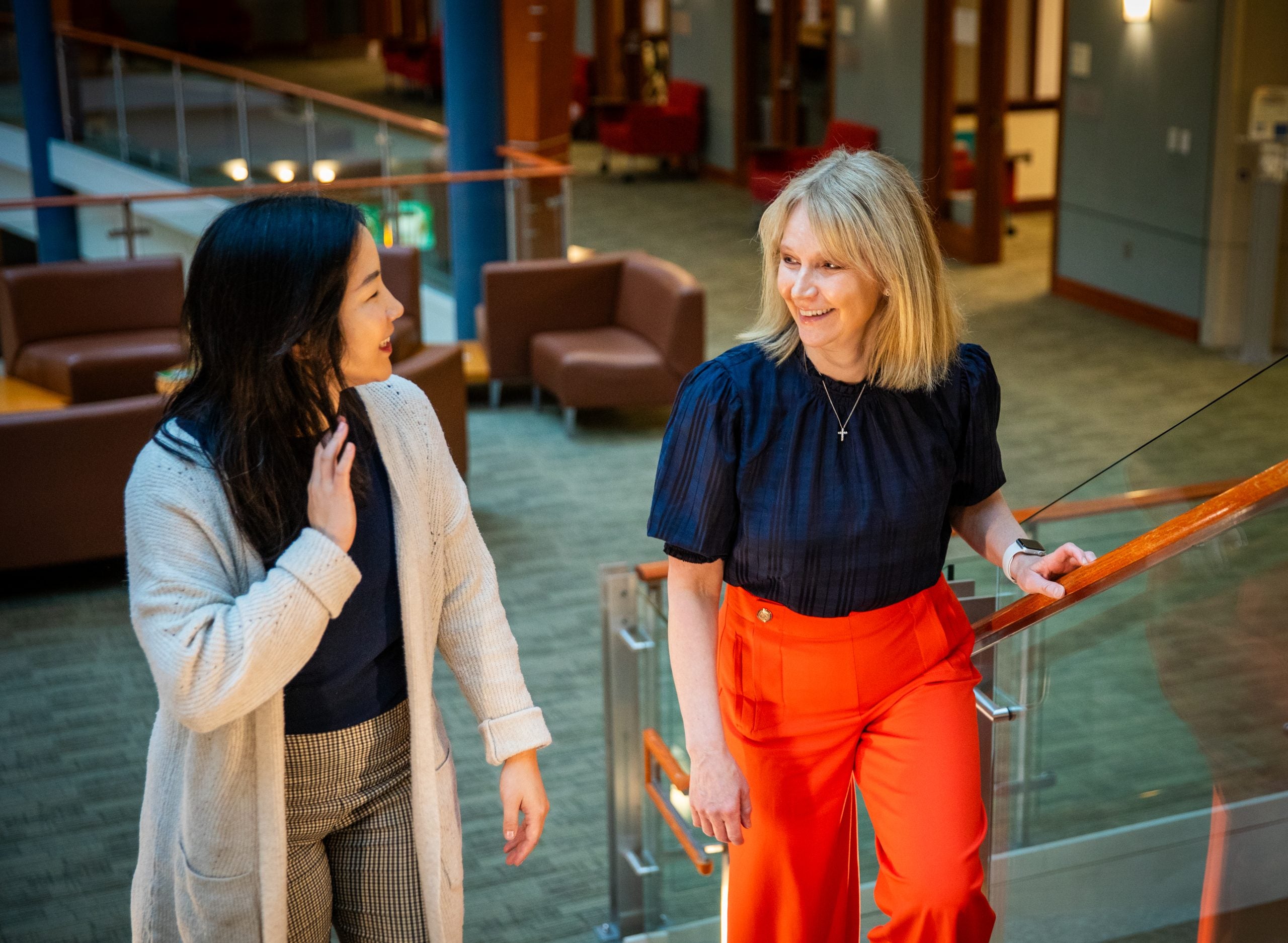 A woman with blonde hair and bright red pants walks up stairs with a student.