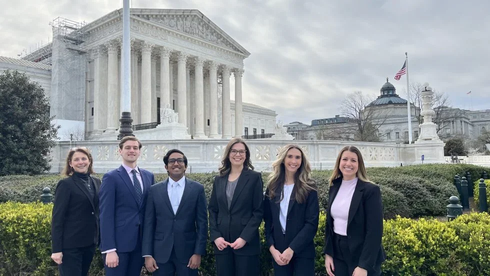 A group of law students stand in front of the columns of the Supreme Court.