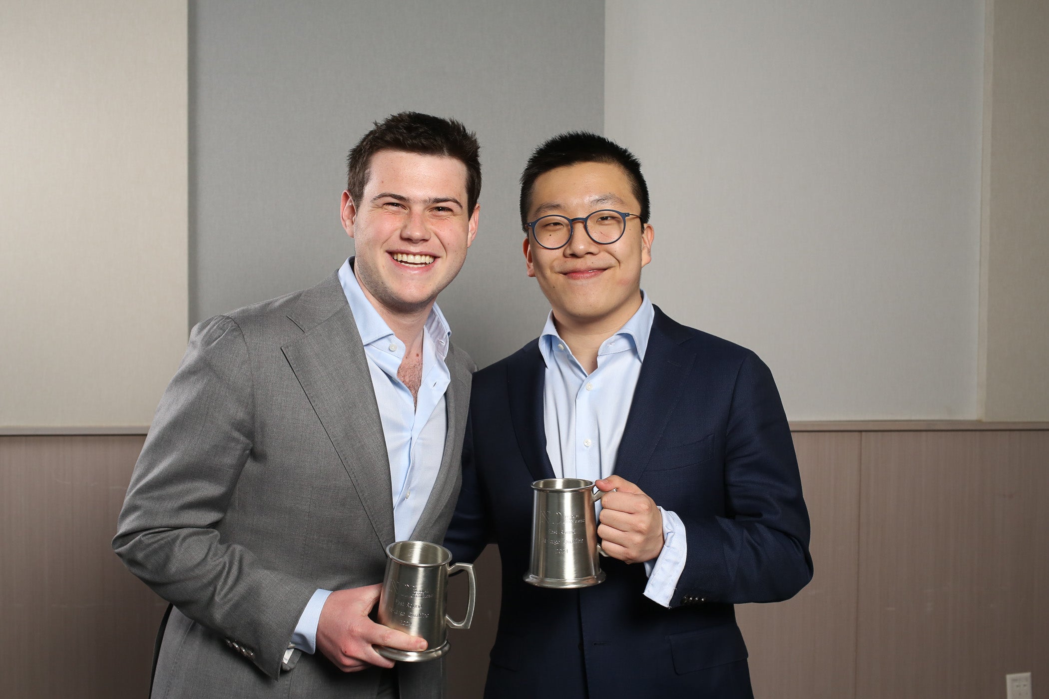 Two male Georgetown students dressed in suits hold metal cups, a prize for a debate tournament.