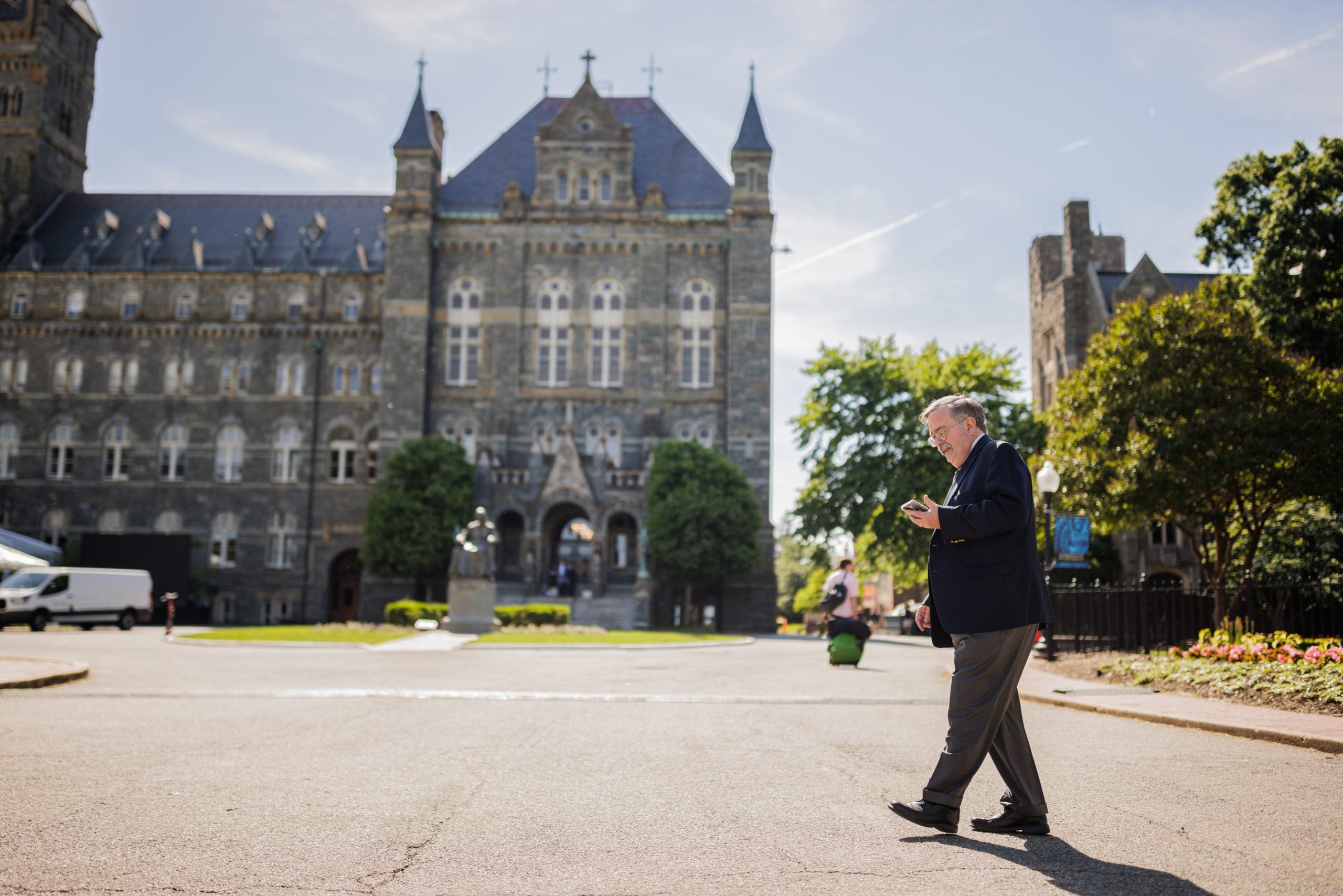 A man with gray hair walks across the entrance to Georgetown and looks at his phone.